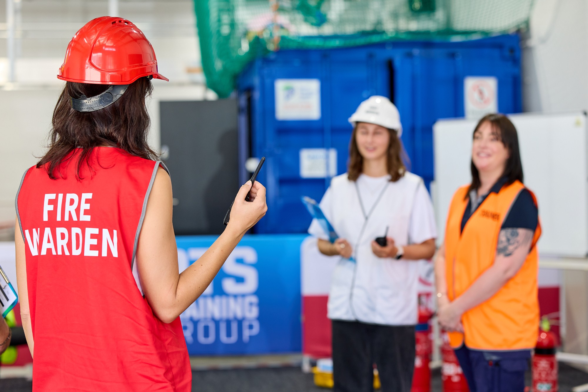 Fire warden in a red vest and helmet leading a training exercise with two participants
